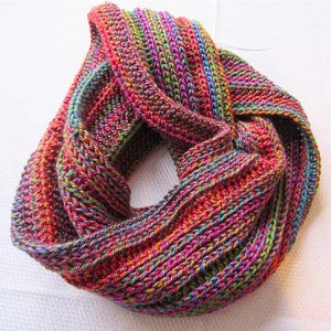 May include: A colorful crocheted infinity scarf with a multi-colored yarn in shades of red, orange, green, blue, and purple.
