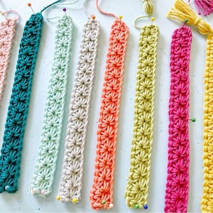 May include: Eight crocheted strips in different colours, including pink, teal, light blue, beige, orange, yellow, hot pink, and green. The strips are pinned to a white surface.