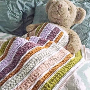 May include: A striped crocheted blanket in shades of purple, brown, white, pink, orange, and green. The blanket is draped over a stuffed teddy bear.