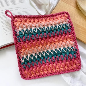 May include: A colorful crocheted pot holder with a pink, orange, and teal striped pattern. The pot holder has a loop handle.