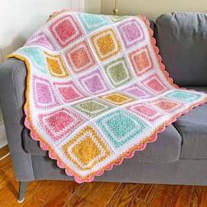 May include: A crocheted blanket with a scalloped edge and a colourful square pattern in shades of pink, green, yellow, and white.