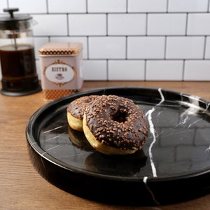 May include: Two chocolate frosted donuts with sprinkles on a black and white marble serving tray.