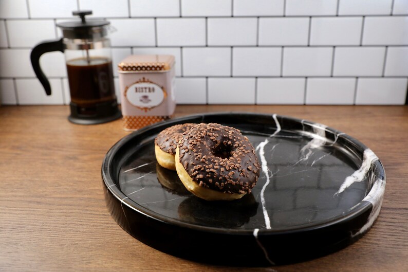 May include: Two chocolate frosted donuts with sprinkles on a black and white marble serving tray.