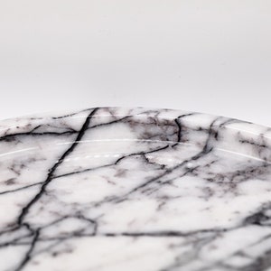 May include: A white marble tray with black veining. The tray is oval shaped and has a slightly raised edge.