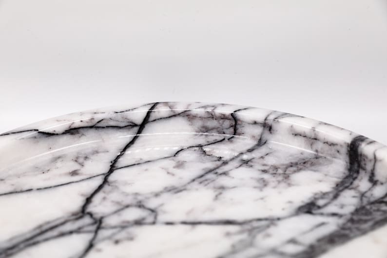 May include: A white marble tray with black veining. The tray is oval shaped and has a slightly raised edge.