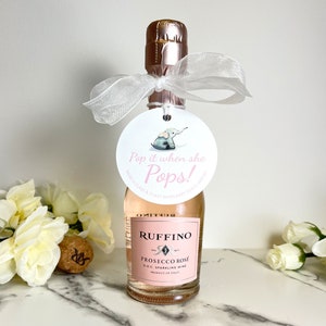May include: A small bottle of pink sparkling wine with a white ribbon and a round tag attached. The tag has a pink and blue elephant illustration and the text 'Pop it when she Pops! Raise a glass & toast when baby girl arrives.'
Pop It When She Pops Personalized Baby Shower Mini Champagne Bottle Favor Tag Prosecco Elephant Gift Tag Custom Baby Shower Gift Tag