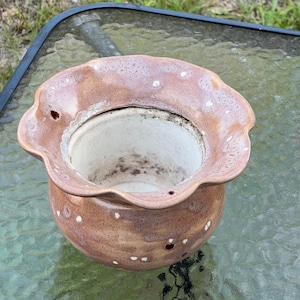 May include: A brown ceramic flower pot with a ruffled rim and a speckled design. The pot has a wide opening and a round base. The interior is white, and the exterior is a mottled brown with white spots.