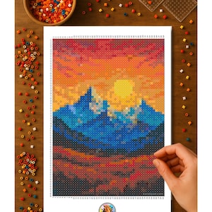 May include: A colorful pixel art landscape featuring mountains under a sunset sky. The artwork is composed of small, colorful beads, with a hand placing a bead. A wooden bowl and other craft supplies are scattered around the artwork.