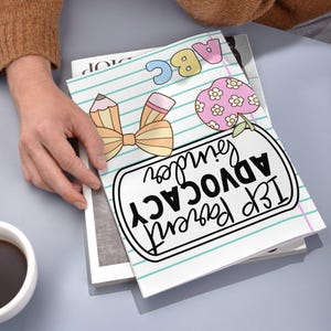 May include: A notebook with a school theme, featuring a pencil and bow illustration, an apple with flowers, and the text "IEP Parent Advocacy". The notebook is open, revealing lined paper with blue lines.