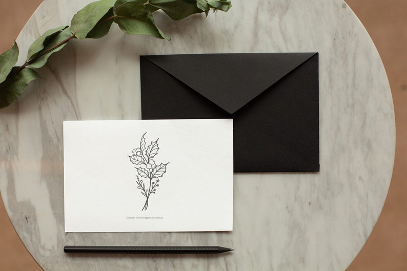 May include: A white card with a black line drawing of a holly sprig on a marble surface with a black envelope and a black pencil.