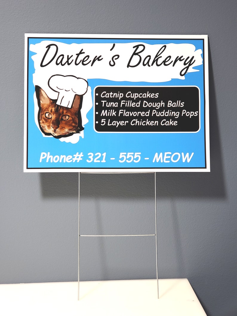May include: A blue and white sign for Daxter's Bakery, featuring a cat wearing a chef's hat. The sign lists cat-themed treats like catnip cupcakes and tuna-filled dough balls. The phone number is 321-555-MEOW.