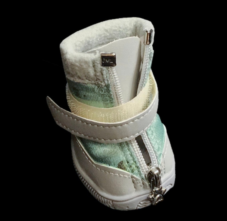 May include: White dog boots with a zipper closure and a green and white patterned lining. The boots have a velcro strap and a JML logo on the side.