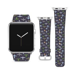 Puede incluir: Un Apple Watch plateado con una correa negra que presenta un patrón repetitivo de aviones coloridos. La esfera del reloj es negra con manecillas blancas.