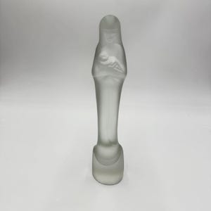 May include: A frosted glass sculpture of a woman holding a baby. The figure is elongated with a rounded base and a detailed depiction of the woman and child. The sculpture is a soft, translucent white.