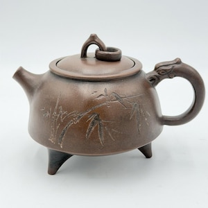 以下が含まれることがあります： 蓋と龍の形をした取っ手が付いた茶色のセラミックティーポット。 ティーポットには3つの小さな脚と竹の葉のエッチングがあります。 注ぎ口は左側にあり、ハンドルは右側にあります。 蓋にはループハンドルが付いています。