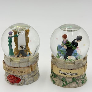 May include: Two snow globes depicting scenes from a fantasy story. One shows a mirror with figures, labelled "Mirror of Erised." The other shows figures entangled, labelled "Devil's Snare." Both have stone-effect bases.