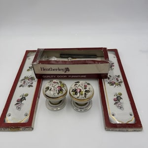 May include: A set of Heatherley door hardware, including two white porcelain doorknobs with floral designs and matching backplates. The packaging reads "QUALITY DOOR FURNITURE" and "22A APPLE BLOSSOM (White)".