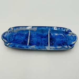 May include: A handmade, ceramic serving dish with three compartments. The dish is a deep blue color with a crystalline pattern and a glossy finish. The edges are slightly raised and have a wavy design.
