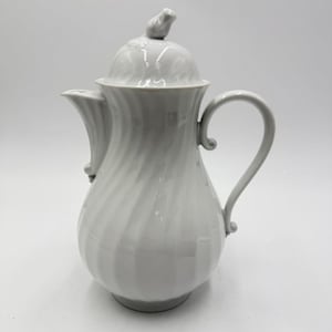 May include: A white ceramic coffee pot with a lid and a curved handle. The pot has a spiral design and a small bird-shaped knob on the lid. The spout is curved and the pot sits on a round base.