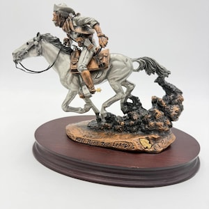 May include: A detailed sculpture of a rider on horseback, crafted in silver and bronze tones. The rider, wearing a hat and period clothing, is depicted in motion. The sculpture is mounted on a dark wooden base, with the text "Hell Bent For Letters".