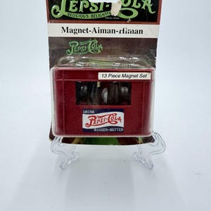 May include: A vintage Pepsi-Cola magnet set in its original packaging. The packaging is a mix of red, black, and white, with the Pepsi-Cola logo. The set includes 13 magnets. The text on the packaging reads "Delicious Delightful" and "Bigger-Better."