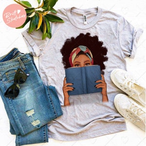 May include: A gray t-shirt with a graphic of a woman with an afro hairstyle wearing a colorful headscarf and holding a blue book in front of her face.
