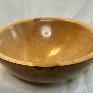 May include: A handcrafted wooden bowl with a natural, light brown finish. The bowl has a smooth, rounded interior and a slightly darker exterior. The wood grain is visible, adding to its rustic charm. This decorative bowl is ideal for serving or display.