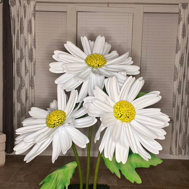 May include: Three large white daisies with yellow centers. The flowers are arranged in a bouquet and have green leaves.