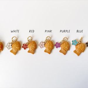 May include: A collection of Taiyaki-shaped charms in various colors, including white, red, pink, purple, blue, and black. Each charm has a gold-colored ring and a small flower or bell accent. The word "BELL" is written above the first charm.