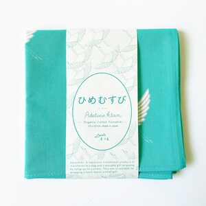 May include: A turquoise blue cotton fabric square with a white crane design and a label that reads "ひめむすび Adeline klam Organic Cotton Furoshiki 50x50cm Made in Japan".