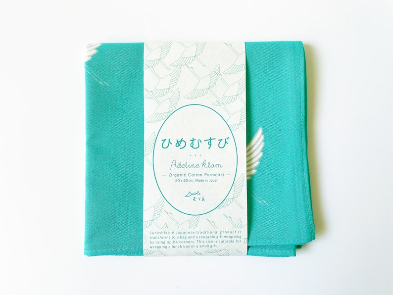 May include: A turquoise blue cotton fabric square with a white crane design and a label that reads "ひめむすび Adeline klam Organic Cotton Furoshiki 50x50cm Made in Japan".