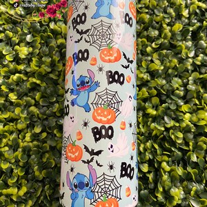 K&ouml;nnte beinhalten: Ein hellblauer Becher mit einem Halloween-Motiv. Das Design zeigt eine blaue Comicfigur, K&uuml;rbisse, Flederm&auml;use, Maisbonbons und Spinnweben. Der Text "BOO" wird im gesamten Design wiederholt.