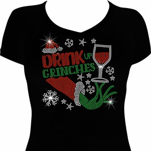 May include: Black t-shirt with a red and green rhinestone design featuring a Grinch hand, a Santa hat, a glass of wine, and the text "Drink Up Grinches".