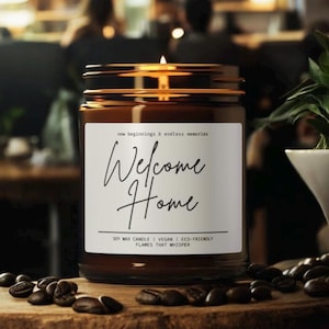 Puede incluir: Un tarro de vela de vidrio marrón con una etiqueta blanca que dice "Welcome Home". La etiqueta también dice "Soy Wax Candle | Vegan | Eco-Friendly Flames That Whisper".