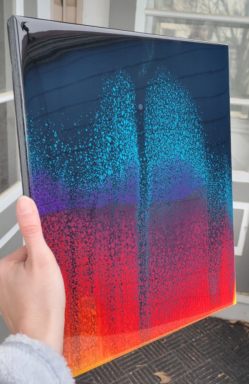 May include: Abstract art painting on a canvas with a black background and a gradient of blue, purple, red, orange, and yellow colours. The paint has a speckled texture.