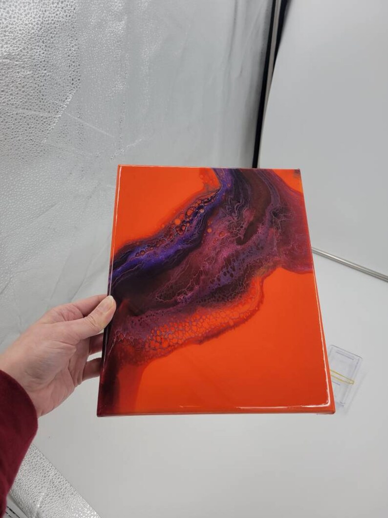 Puede incluir: Pintura abstracta sobre lienzo con un fondo naranja brillante y un dise&ntilde;o de remolino morado y negro.