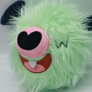 Puede incluir: Un peluche con un exterior de piel verde claro y peluda. El juguete presenta una nariz rosa con un centro negro en forma de coraz&oacute;n, una boca marr&oacute;n con un diente blanco y orejas azul oscuro. Una 'W' verde est&aacute; cosida en el lateral.
