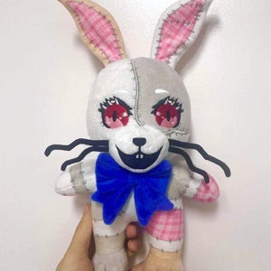 May include: A white and gray plush rabbit toy with pink ears and a blue bow. The toy has red eyes and a stitched-together appearance.