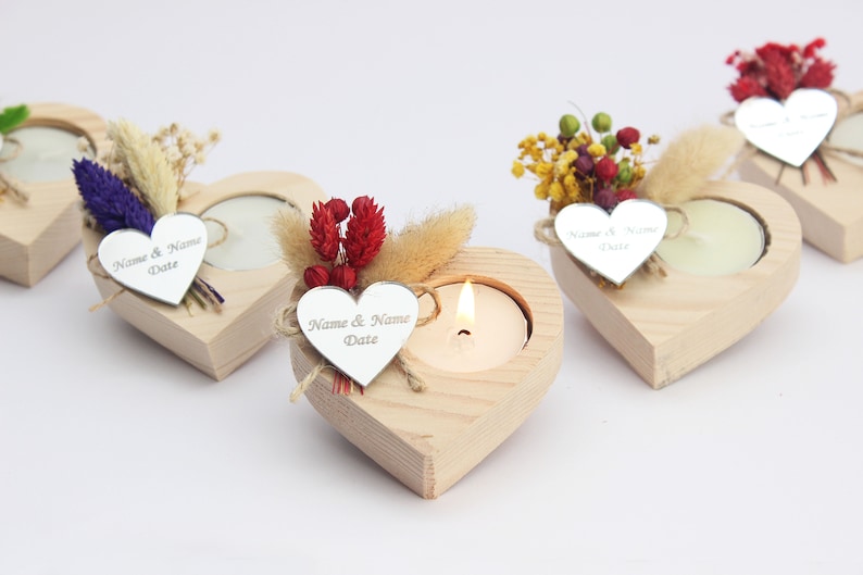May include: Set of four wooden heart-shaped candle holders with a small tea light candle in each. Each holder is decorated with dried flowers and a silver heart-shaped tag with the text "Name & Name Date".
