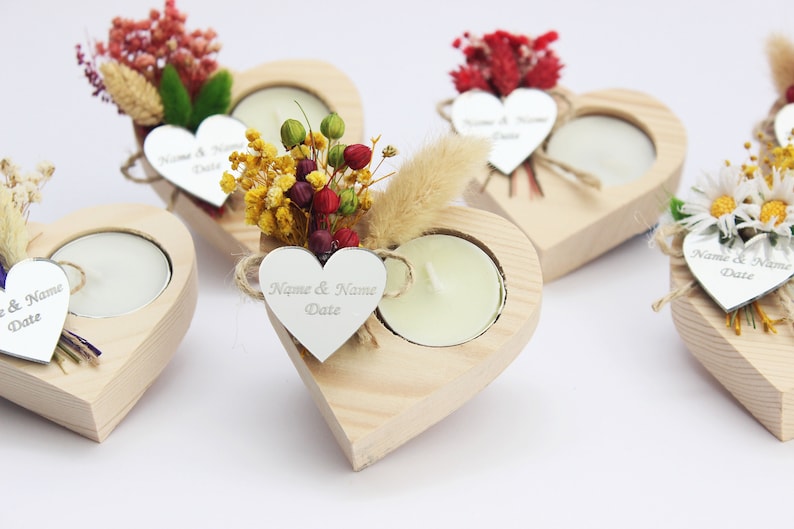 May include: Set of four wooden heart-shaped candle holders with a small tea light candle in each. Each holder is decorated with dried flowers and a silver heart-shaped tag with the text "Name & Name Date".