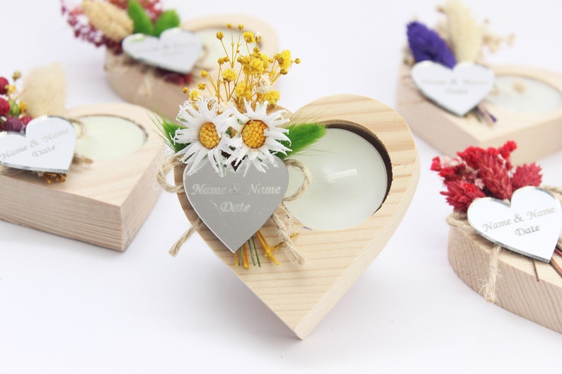 May include: Wooden heart-shaped candle holders with a small tea light candle in each. The holders are decorated with dried flowers and a silver heart tag with the text "Name & Name Date".