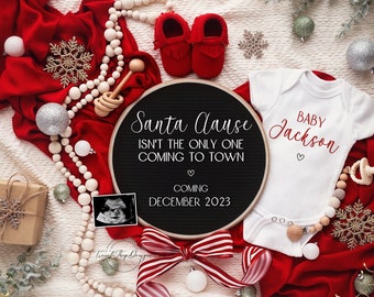 May include: A white onesie with the text "BABY Jackson" in red script. A black chalkboard sign with the text "Santa Clause isn't the only one coming to town" and "Coming December 2023". The sign is surrounded by a white beaded garland, a red and white striped ribbon, a small gift box, a white snowflake, and a pair of red baby booties.