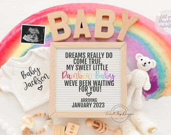Pode incluir: Um fundo de aquarela em arco-íris com um macacão branco que diz "Baby Jackson" e um urso de pelúcia branco de crochê. Uma placa diz "Dreams really do come true, my sweet little Rainbow Baby. We've been waiting for you! Arriving January 2023".
