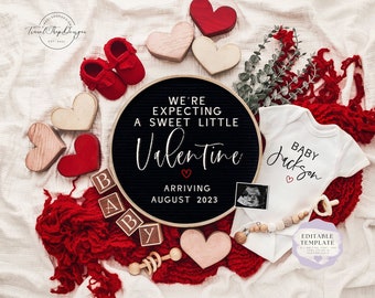 May include: A black chalkboard sign with the text "We're expecting a sweet little Valentine arriving August 2023".  The sign is surrounded by red and pink hearts, a baby onesie with the text "Baby Jackson", and wooden blocks that spell out "Baby".