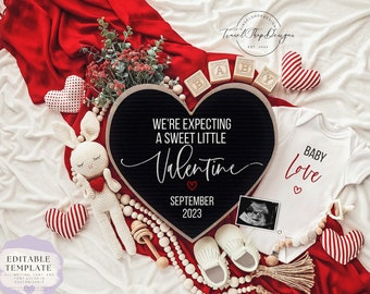 Könnte beinhalten: Ein schwarzes herzförmiges Buchstabenbrett mit dem Text "We're expecting a sweet little Valentine September 2023". Das Brett ist umgeben von einer weißen Decke, einer roten Decke, einem weißen Strampler mit dem Text "Baby Love", einem gehäkelten Hasen, Holzperlen und einem Paar Babyschuhe.
