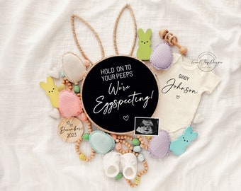 Peut inclure: Une pancarte en ardoise noire avec le texte "Hold on to your peeps We're Eggspecting!" entourée de décorations sur le thème de Pâques, dont un body de bébé avec le texte "Baby Johnson", un lapin en bois et une pancarte en bois avec le texte "December 2023".