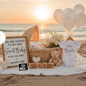 Könnte beinhalten: Strandszene mit einem Weidenkorb, Luftballons und Babykleidung. Ein Schild lautet: "WE ARE EXCITED TO SAY OUR Sweet Baby IS ON THE WAY! JANUARY 2026." Ein weißer Body trägt die Aufschrift "BABY Brooks." Holzblöcke buchstabieren "BABY."