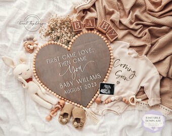 May include: A wooden heart-shaped sign with the text "First came love, then came you" and "Baby Williams August 2023". The sign is surrounded by wooden beads, a baby onesie, a stuffed bunny, and a baby rattle.
