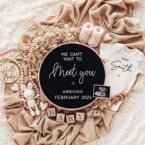 Op de afbeelding: Een baby aankondiging met een zwart rond bord met de tekst "We can't wait to meet you" en "Arriving February 2024." De aankondiging bevat een witte romper met "Baby Smith" erop gedrukt, babyschoentjes, houten blokken met "BABY" en een echo.