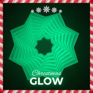 Puede incluir: Un adorno verde en forma de estrella que brilla en la oscuridad con el texto "Christmas GLOW" en la parte inferior.